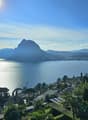 Lake Lugano with mountains in the background, a clear blue sky, town in the distance, greenery