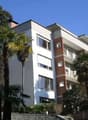 Multi-story apartment building with balconies, surrounded by palm trees and greenery