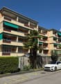 multi-story building, beige exterior, green awnings, balconies, hedges, palm tree, cars parked