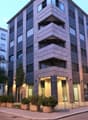 Modern apartment building, multiple floors, glass windows, entrance with lights, shrubs and trees in front