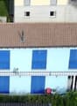 White house with blue shutters, brown roof, raised ground floor, garden