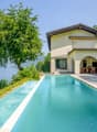 Two-story villa with a swimming pool, surrounded by lush greenery and overlooking a lake. The villa has a terrace and large windows, providing a scenic view of the natural landscape.