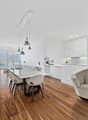 modern interior, hardwood floor, large windows, dining table with chairs, white walls, white cabinets, built-in television, floral vase, modern chandeliers, contemporary armchair, black shelf