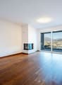 Empty room with hardwood floors, white walls, fireplace, sliding glass doors to balcony, city view.