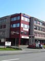 Office building, red facade, multiple windows, multiple floors, signboard, cars parked in front
