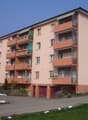4-story apartment building with orange and beige exterior, balconies on each unit, and a parking area in front