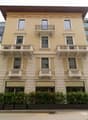 3 story building with beige paint, black iron balconies, window grills, greenery at the bottom