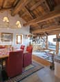 Dining area with dining table, red chairs, fireplace, wood beam ceiling, large windows, wood rocking chair, chandelier