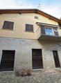 2 story house, stone facade, raised ground floor, balcony, two large wooden doors, stone steps