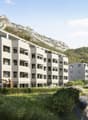 modern multistory building, surrounded by mountains, greenery, car access road, parking spaces