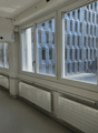 Empty office room with large windows, radiators, grey flooring