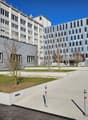 Modern office buildings with glass windows, paved entrance, landscaping, and gray exterior