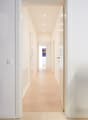 Empty corridor with hardwood floor, white walls, recessed ceiling lighting.