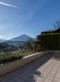 Outdoor terrace with tiled flooring, surrounded by greenery and a view of the mountains.