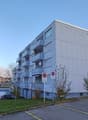 large building with many balconies, white walls, multiple floors, and parking lot in front