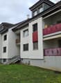 Multi-story apartment building with white exterior walls, red and yellow accents, and balconies with red railings.
