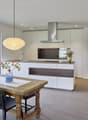 Modern kitchen with dining area, large windows, wooden floor, table and chairs, hanging lamp, stainless steel range hood, flowers in vase