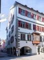 Three story commercial building, red shutters, central arched entrance, shops on the ground floor
