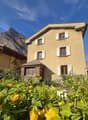 two-story stone house, white shutters, large flower beds with yellow flowers, stunning mountain views