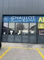Commercial building, gray walls, large glass doors, parking area in front, signage in French