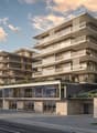 Multi-story apartment building with modern, angular design featuring balconies and terraces, ground-level retail space, and parking area in front