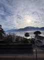 Wide view of a road, lake, mountains, white houses, road, trees, sky with clouds