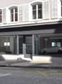 Storefront with glass windows, white shutters, black awning, white car visible inside