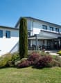 Modern white house with glass windows, a patio with outdoor furniture, and a well-maintained garden.