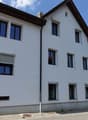 3 story residential building, white facade, multiple windows, brown roof, brick path in front
