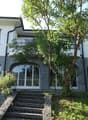 2 story villa, white walls, arched windows, stone base, tree, large balcony, steps, trampoline
