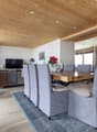 Dining room with wooden table, gray chairs, wooden ceiling, carpet, living room with couch, TV, plants, and a mirror.