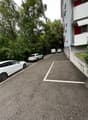 Parking area with three cars parked, asphalt ground, street trees on the side, building on the right.