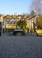 wooden pergola, concrete table, gravel surface, wooden fence