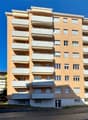 Multi-story apartment building, balconies, large windows, main entrance, exterior parking