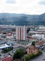 Cityscape with diverse buildings, various greenery, several cars parked, and an urban environment with roads and hills in the background.