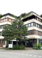 modern office building, beige exterior, brown trim, large windows, trees, cars parked in front