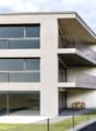 3-story modern apartment building with large windows, balconies, and a small outdoor seating area on the ground floor