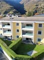 3-story apartment building, yellow exterior, multiple balconies, green hedges, solar panels on the roof, mountain view