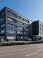 modern office building with multiple windows, concrete facade, ground floor entrance, parking area