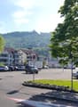 Parking area with multiple cars, residential buildings in the background, trees, flags