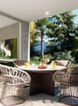 A patio area with a table and chairs, a glass wall, and an open view to a garden