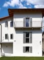 modern white house, brown roof, balcony, windows with shutters, garden, lawn