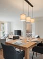 modern dining area with wooden table and chairs, gray sofa, table set for 6, large windows, tv, wooden cabinets