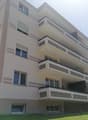 Multi-story apartment building with beige exterior, large windows, and balconies on each floor.