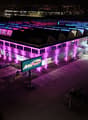 Large commercial building with colorful LED lighting on the exterior, parking lot in the foreground, and a sign for 'Arbor Park' visible.