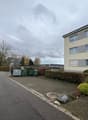 Apartment building, concrete path, shrubs, bushes, trash bins, streetlight, cars driving