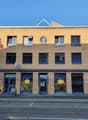 3 story building, blue trim, round windows, commercial windows, 3 entrances, barrel outside, plants