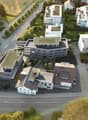 Multi-storey building with multiple terraces, green roofs, and several balconies. Raised ground floor. Street with white markings.