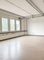 Empty room with white walls, beige floor, large windows, blue door, metal beams on ceiling
