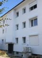 Multi-story building, white exterior, multiple windows, entrance with canopy, some items stored outside